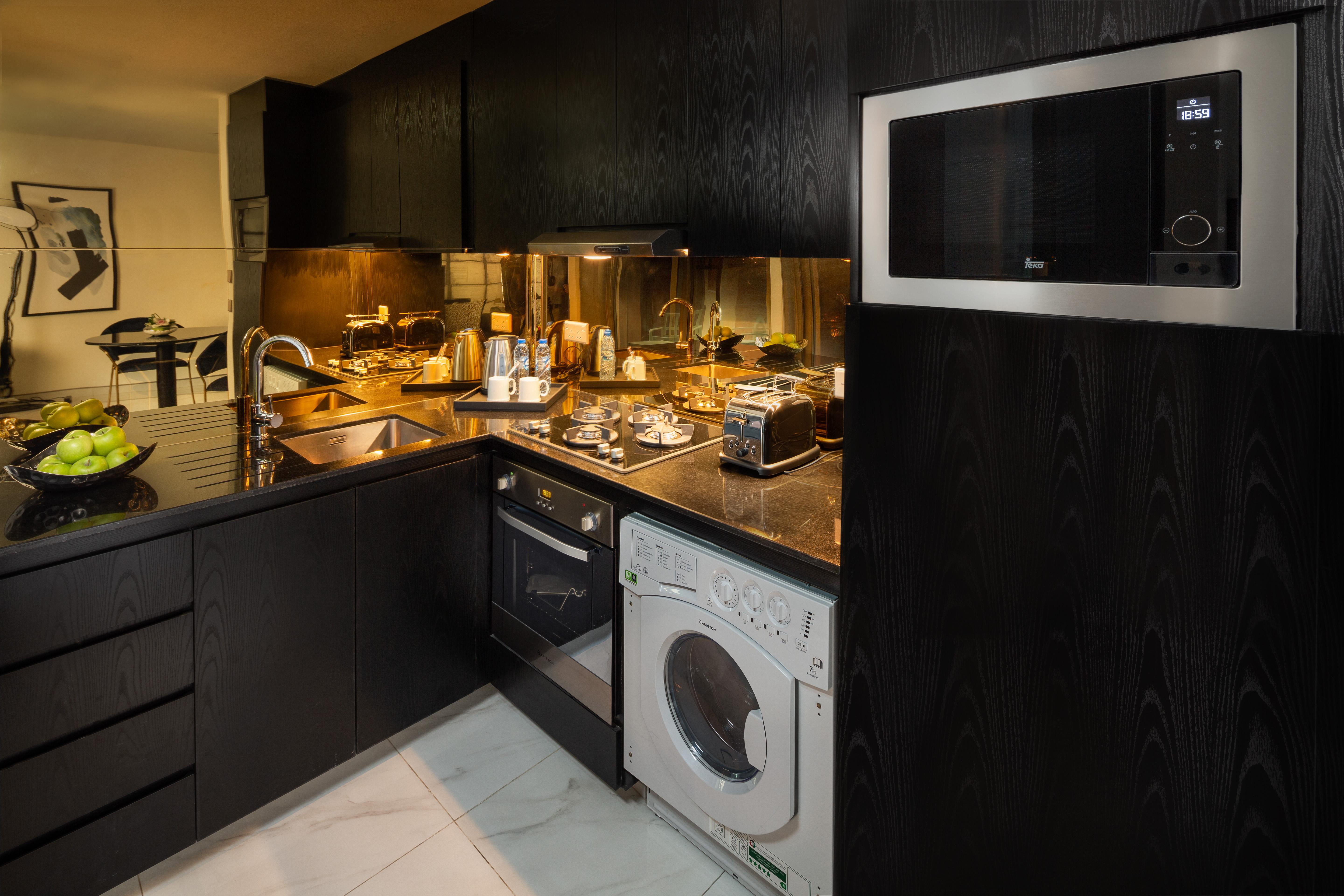 Millennium Atria Business Bay Aparthotel Дубай Екстериор снимка The photo shows a modern kitchen with a sleek design featuring black cabinetry and countertops. There is a sink with a faucet, a stove with multiple burners, and an oven integrated into the cabinetry. A microwave is mounted above the counter for conv