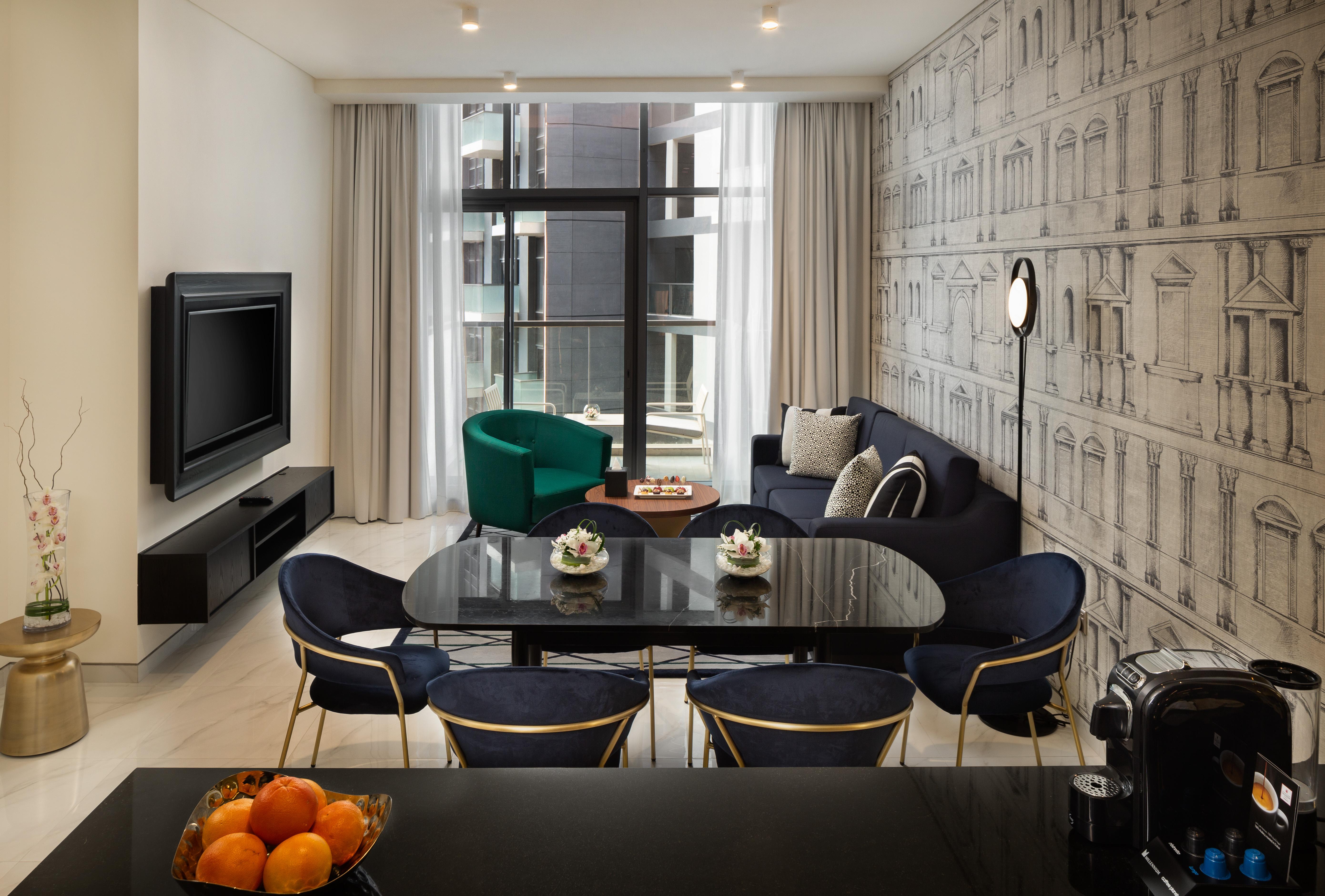 Millennium Atria Business Bay Aparthotel Дубай Екстериор снимка The photo shows a modern living space that includes a cozy seating area and dining setup. On the left, there is a large television mounted on the wall. The living room features a blue sofa and a green accent chair, creating a stylish contrast. A smal