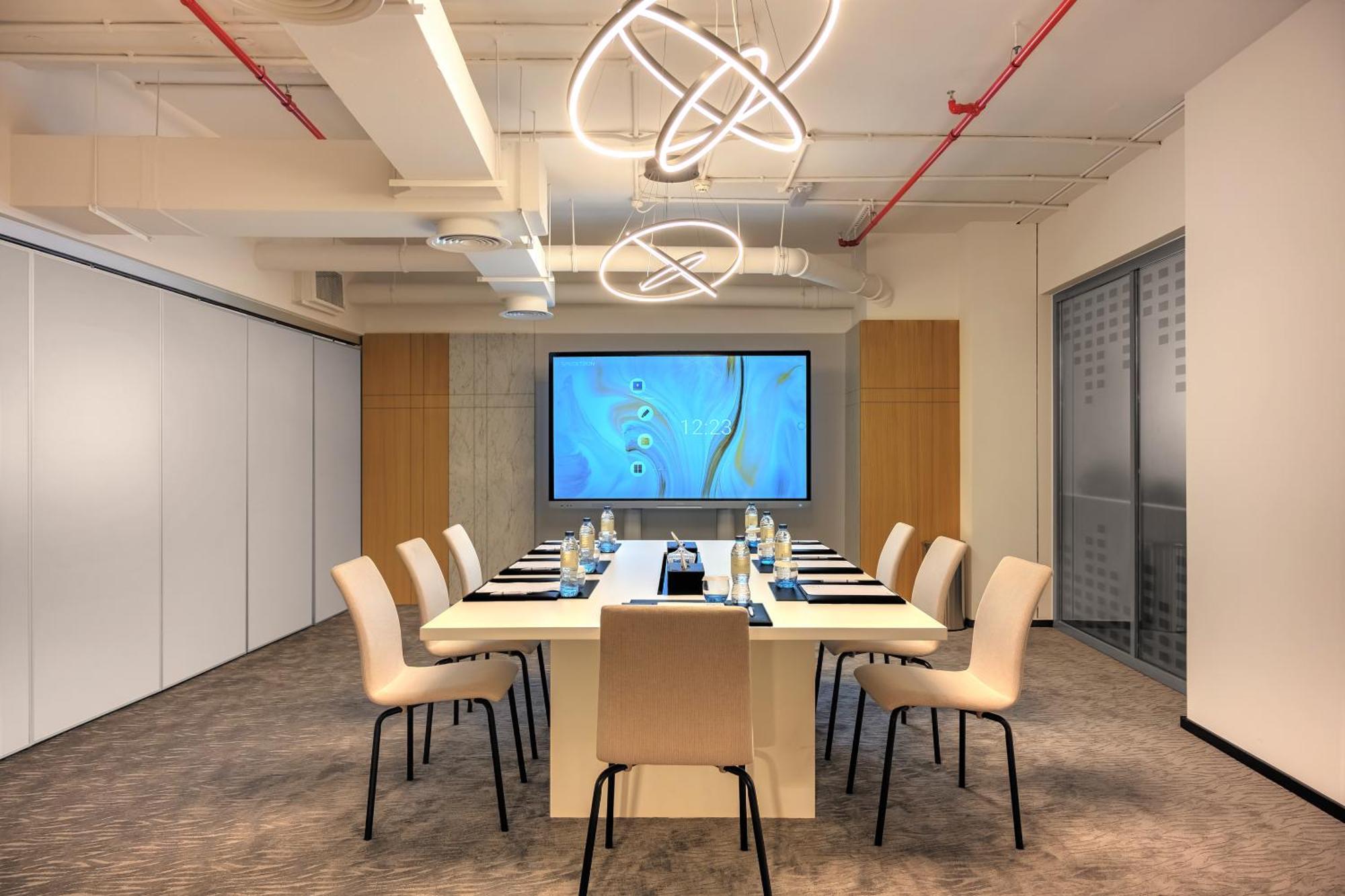Millennium Atria Business Bay Aparthotel Дубай Екстериор снимка The photo shows a modern conference room designed for meetings. It features a long white table surrounded by beige chairs. At the end of the table, there is a large screen displaying a blue abstract design. The room is well-lit with contemporary ligh