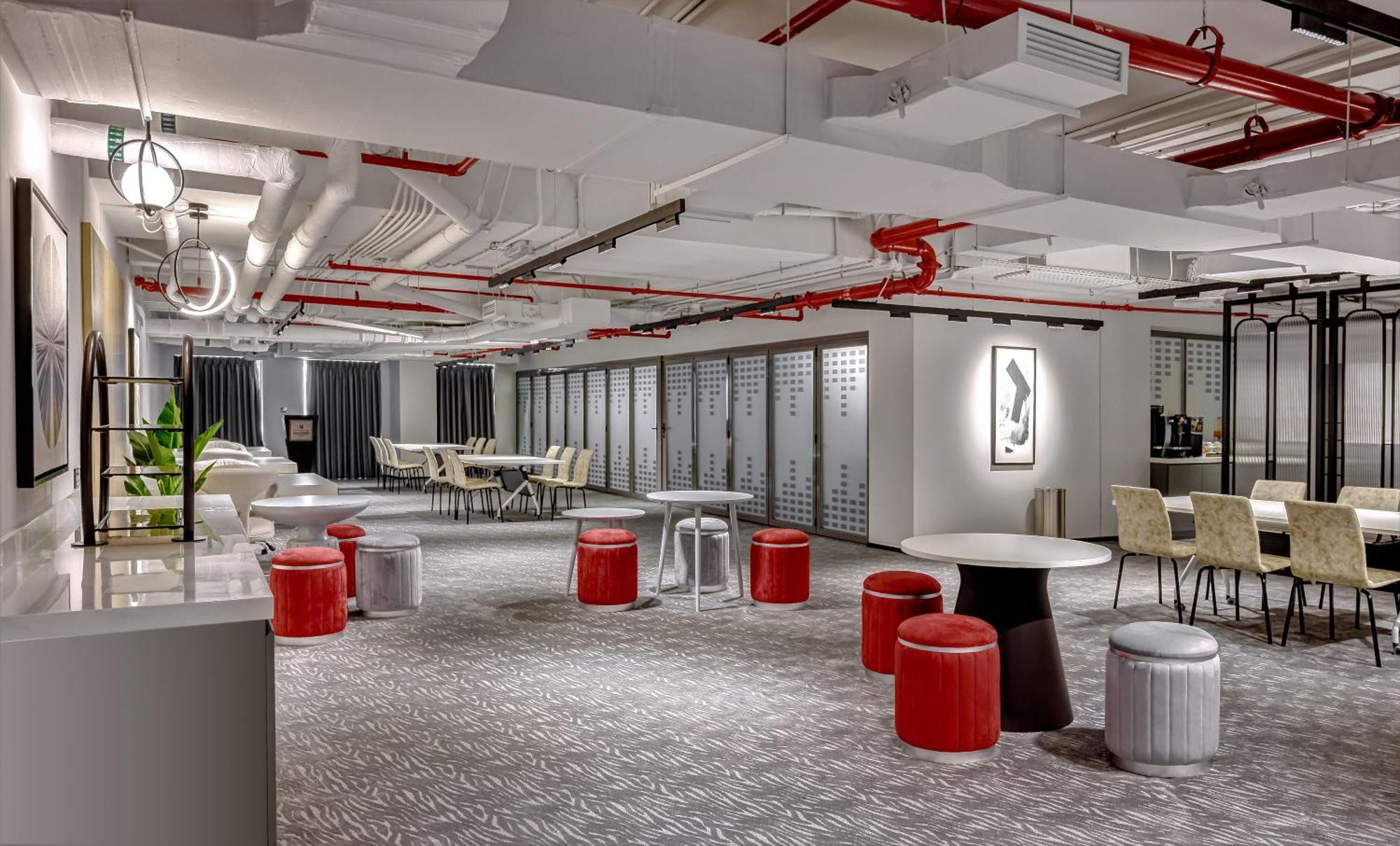Millennium Atria Business Bay Aparthotel Дубай Екстериор снимка The photo shows a modern interior space, likely an office or communal area. The flooring is covered with a textured carpet, and the ceiling features exposed pipes painted red. 

There are several seating options, including small round tables with sto