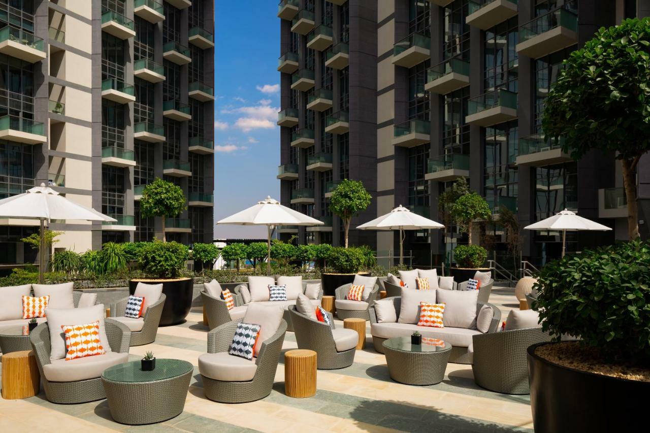 Millennium Atria Business Bay Aparthotel Дубай Екстериор снимка The photo shows a modern outdoor lounge area, featuring several comfortable seating arrangements made of soft, stylish lounge chairs and round tables. The seating is adorned with colorful pillows, adding a pop of color to the neutral tones of the fur