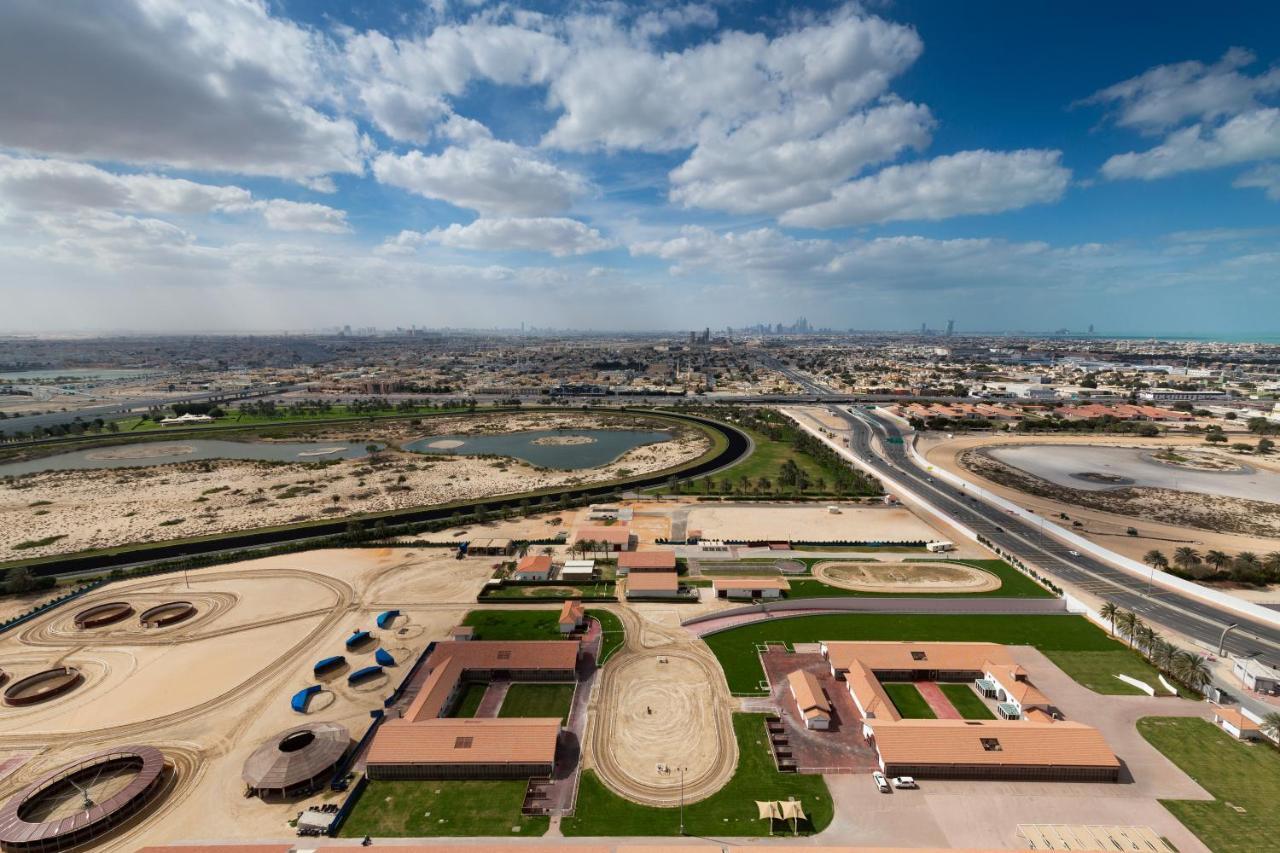 Millennium Atria Business Bay Aparthotel Дубай Екстериор снимка The photo shows a panoramic view of a large landscape with expansive open areas, buildings, and a curved track. In the foreground, there are several stable structures and facilities associated with horse training or racing, surrounded by well-maintai