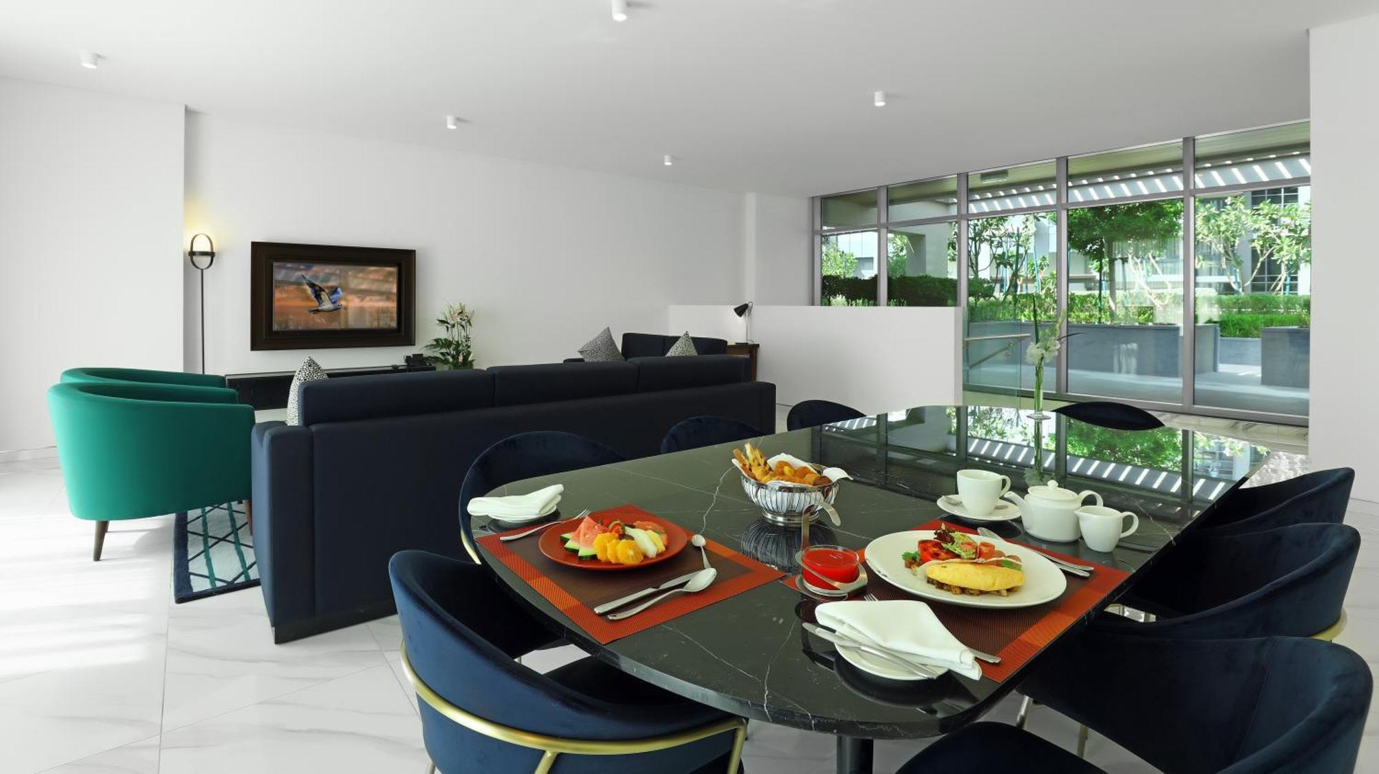 Millennium Atria Business Bay Aparthotel Дубай Екстериор снимка The photo depicts a modern living space with a dining area and a seating area. In the foreground, there is a round dining table set with plates of food, including eggs, toast, and a small bowl of fruit, accompanied by cups and napkins. The table is c